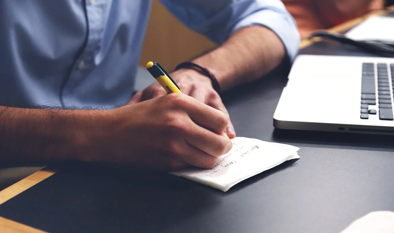 A person writing notes beside a laptop